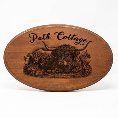 Personalised laser engraved oval Highland Cow house sign handcrafted in mahogany – custom cottage name in script with wildflower illustration, Moon Groves UK
